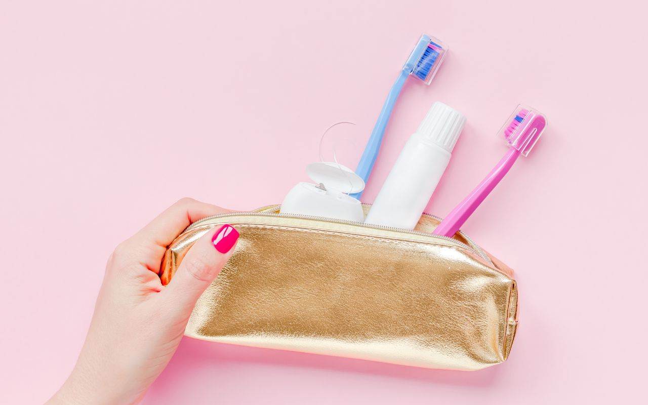 A woman's hand holding a gold cosmetic bag filled with toothbrushes and toothpaste, providing Christmas dental tips.