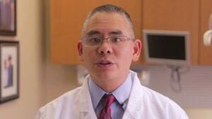 A dentist with dental implants wearing glasses and a lab coat in a dental office.