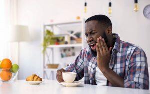 A man is sitting at a table with a cup of coffee, potentially experiencing dental issues.