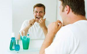 A man practicing dental hygiene by brushing his teeth in front of a mirror.