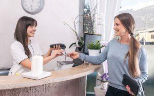 A woman is handing a credit card at a reception desk while discussing the difference between restorative and cosmetic dentistry.