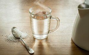 A home remedy for toothache involving a cup of water and a spoon on a wooden table.