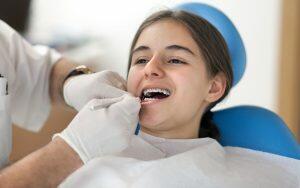 A young girl having her teeth checked by a dentist after braces brackets fall off.