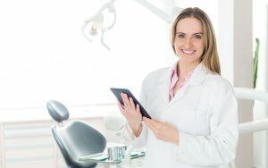 A female dental hygienist holding a tablet in front of a dental chair during Dental Hygienists' Week.