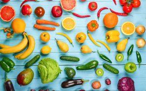 A variety of fruits and vegetables are arranged on a blue background.