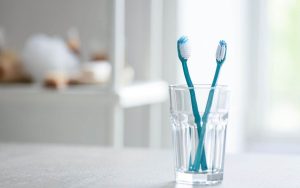 Two blue toothbrushes in a glass on a table.