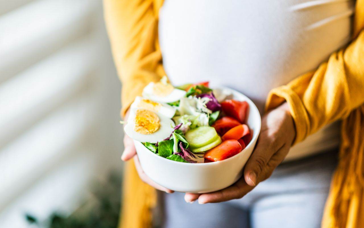 A pregnant woman holding a bowl of salad.