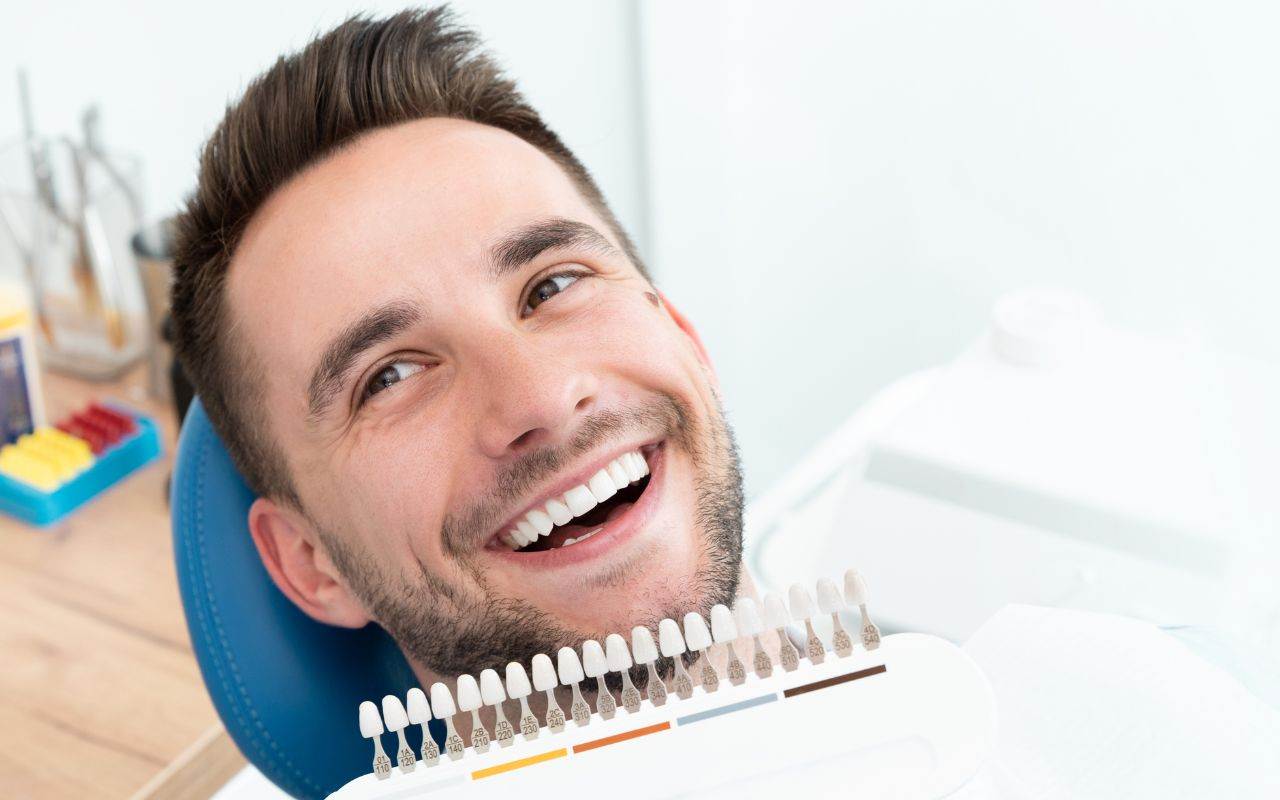 pros-and-cons-of-professional-teeth-whitening-compared-to-at-home-kits - A man smiles while undergoing professional teeth whitening at a dentist's chair.