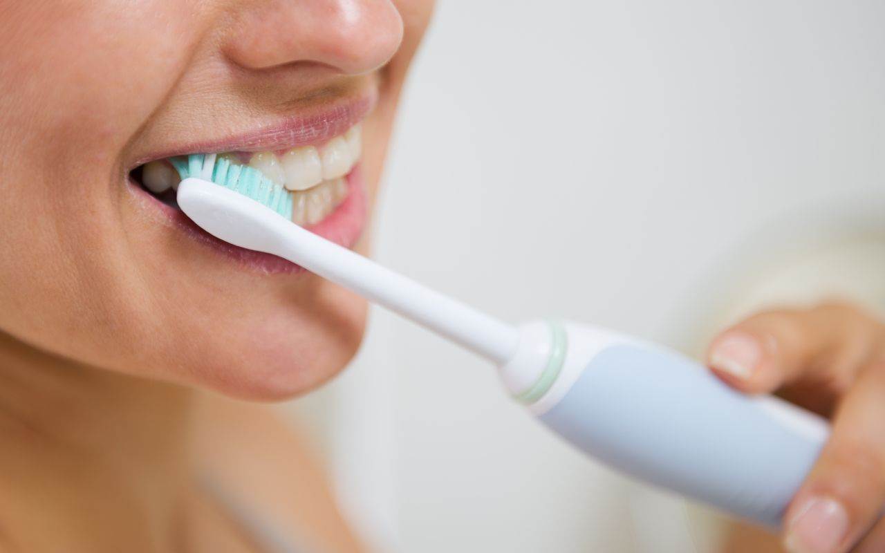 A woman is brushing her teeth with an electric toothbrush.