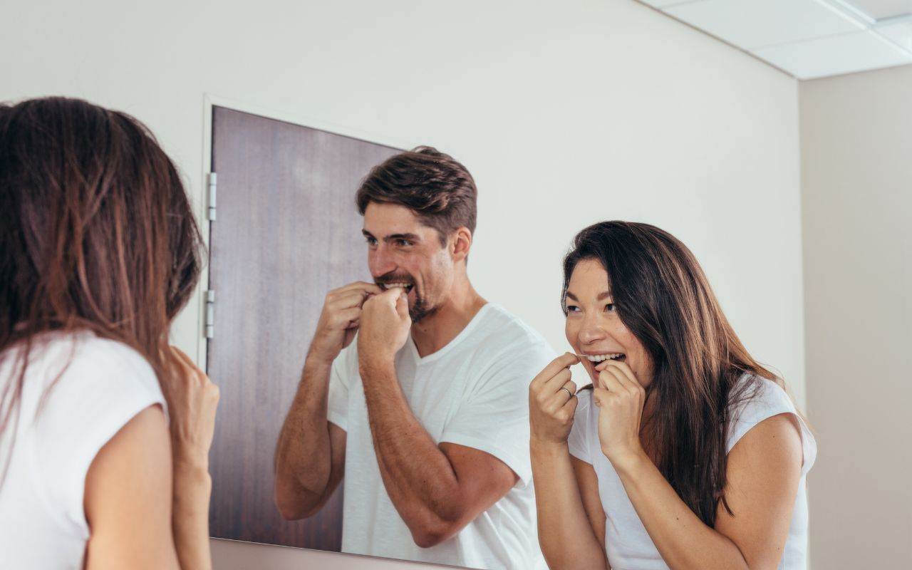 A man and woman brushing teeth in front of a mirror - focus-on-oral-hygiene-to-maintain-balanced-oral-microbiome