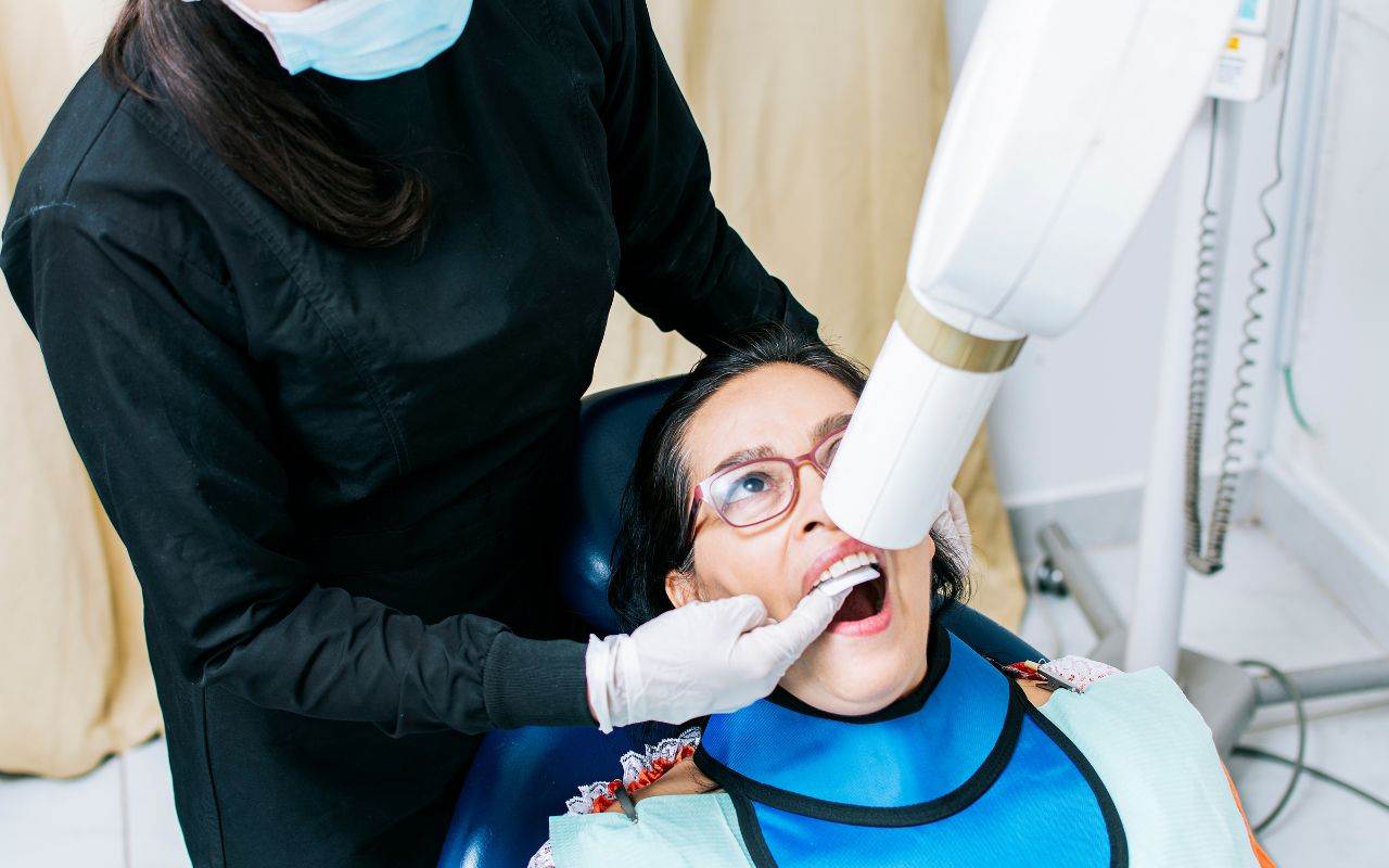 A woman is getting her teeth examined by a dentist with a dental x-ray machine